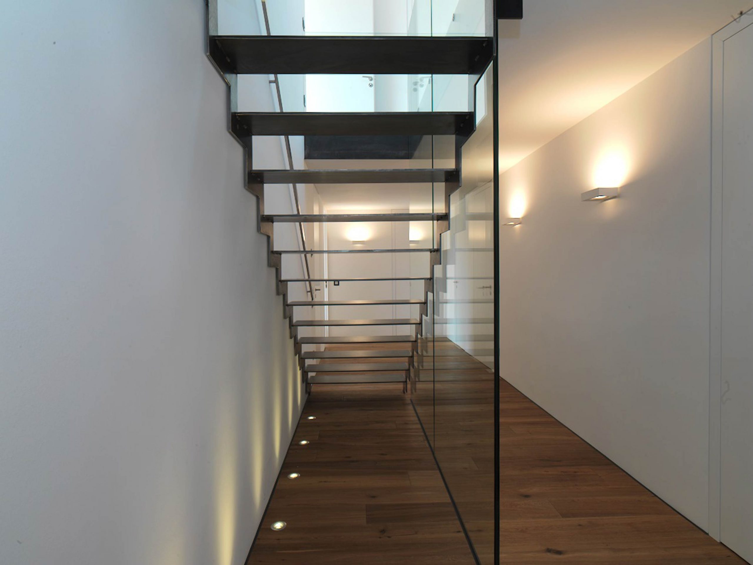 Die neue freitragende Stahltreppe mit Stufen aus geflammten Stahl und Bodenstrahlern im Einfamilienhaus 