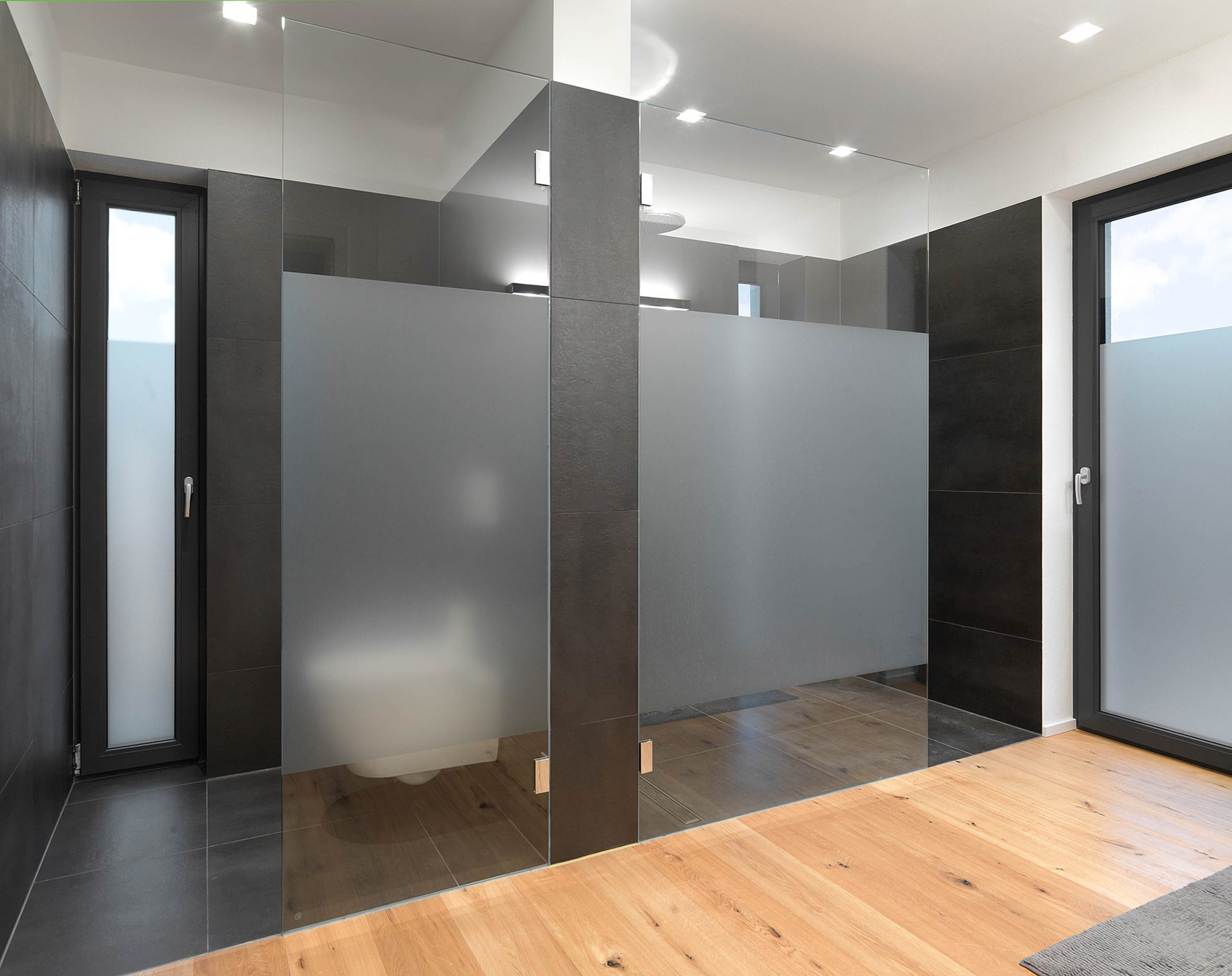 Der Dusch- und WC Bereich mit anthrazitfarbenen Fliesen und hellem Echtholzfußboden im Bad von Einfamilienhaus 