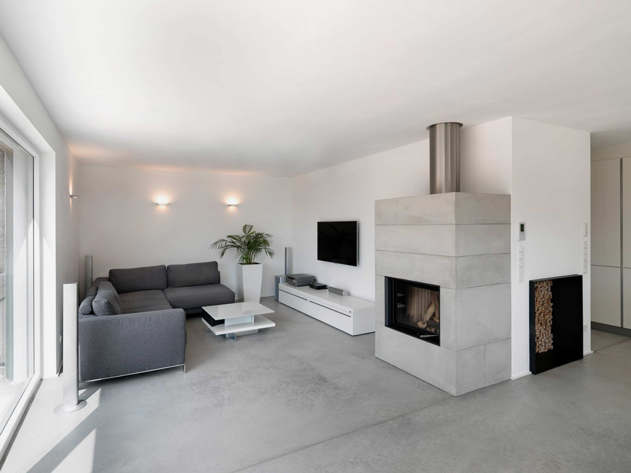 Der Wohnbereich mit Sichtbeton-Kamin und fluegelgeglaettetem Estrich im Einfamilienhaus 