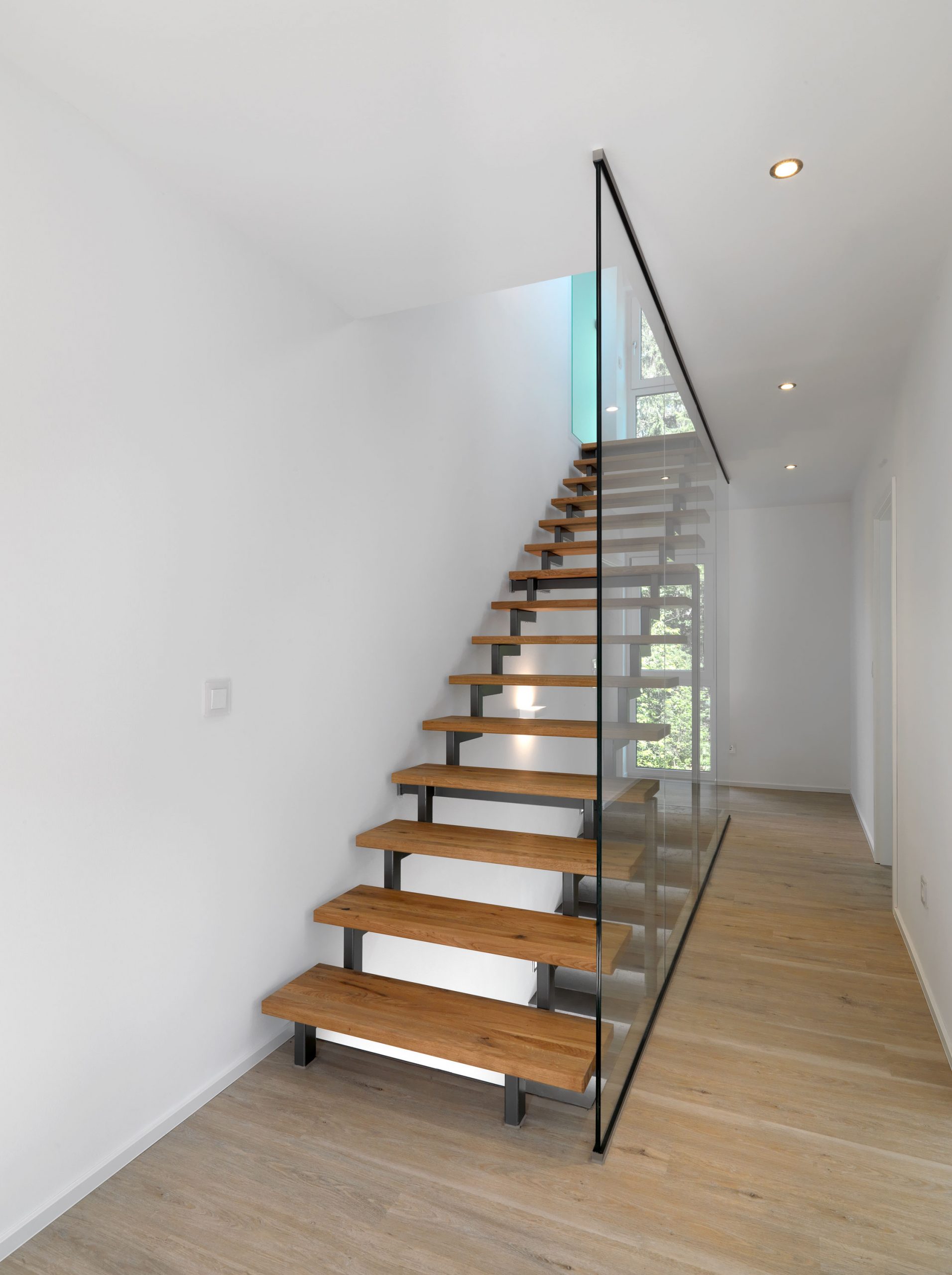 Die setzstufenlose gerade Treppe auf zwei Stahlholmen abgetrennt vom Flur durch feste Glaselemente.